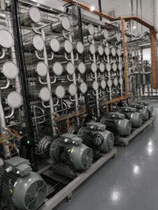Por: Juçara Pivaro Nesse cenário, a TecnoQuímica, com 30 anos de atuação no setor de higienização, é especializada no fornecimento de soluções químicas para processos industriais, concentra parte de sua atuação no desenvolvimento de alternativas para limpeza e manutenção de sistemas de processamento. Com know-how técnico em higienização industrial, especialmente nos processos de Cleaning in Place (CIP) e tratamento de água, a empresa combina o fornecimento de produtos com assistência técnica de campo e suporte à otimização dos processos. No setor lácteo, entre as principais frentes estão a limpeza de membranas utilizadas em sistemas de filtração e concentração e o uso de aditivos para aumentar a eficiência dos ciclos de CIP. Uma das novidades destacadas pela TecnoQuímica é a linha Divos ACP, da Diversey, desenvolvida para a limpeza e manutenção de sistemas de filtração por membranas, como ultrafiltração (UF) e nanofiltração (NF). A solução é formada por três produtos: Divos ACP B1, detergente líquido à base de tensoativos e indicado para diferentes condições de dureza da água; Divos ACP E1, detergente líquido à base de enzimas e isento de tensoativos; e Divos ACP D1, aditivo líquido alcalino de alta atividade. De acordo com Carlos Ciola, gerente da empresa, a linha oferece flexibilidade para diferentes aplicações e pode contribuir para reduzir etapas dos ciclos de limpeza, além do consumo de água, produtos químicos e tempo de operação. A linha preserva ainda a integridade das membranas, importante para a vida útil dos componentes e para proteção dos investimentos dos laticínios Outra frente de atuação é o conceito CIP Single Stage, que tem como principais produtos o Kompleet e o Complex. Os aditivos, formulados com sequestrantes e tensoativos, são utilizados para potencializar a ação das soluções ácidas e alcalinas empregadas nos processos de higienização. A TecnoQuímica também atua no tratamento de água e efluentes, fornecendo coagulantes, floculantes, polímeros e produtos para correção de pH. A empresa trabalha na otimização dos sistemas já instalados nas plantas industriais, com suporte técnico para ajustes de dosagem, ponto de aplicação, tempo de mistura e outros parâmetros operacionais. A proposta é reduzir custos e contribuir para que o efluente tratado atenda aos parâmetros de lançamento exigidos pela legislação, associando eficiência operacional, segurança e uso mais racional.